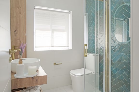 Baño moderno con ducha de vidrio, lavabo sobre mueble de madera y azulejos en tonos verdes.