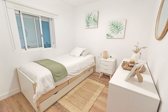 Dormitorio minimalista con cama individual, muebles blancos y decoración en tonos verdes.