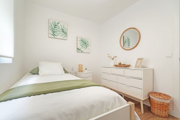 Habitación luminosa con cama individual, decorada con plantas y mueble blanco.