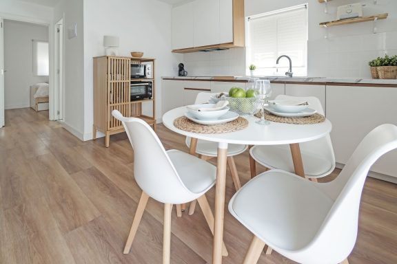 Mesa blanca con sillas, decorada con vajilla, en una cocina moderna y luminosa.