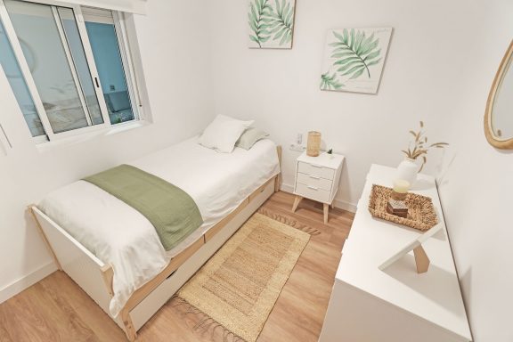Habitación minimalista con cama, mesita, y decoraciones de plantas. Suelo de madera clara.