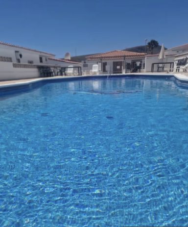 Piscina con agua clara y azul, rodeada de edificios bajo un cielo despejado.