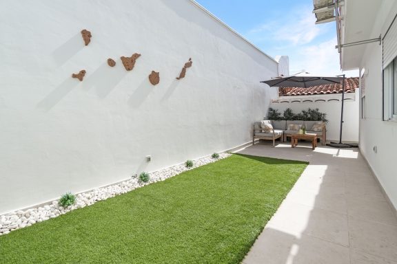 Patio moderno con césped artificial y decoración en la pared, mesas y sillas de exterior.