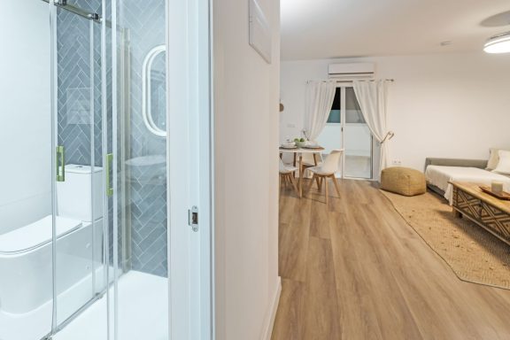 Vista de un baño moderno y una sala de estar luminosa con muebles claros.