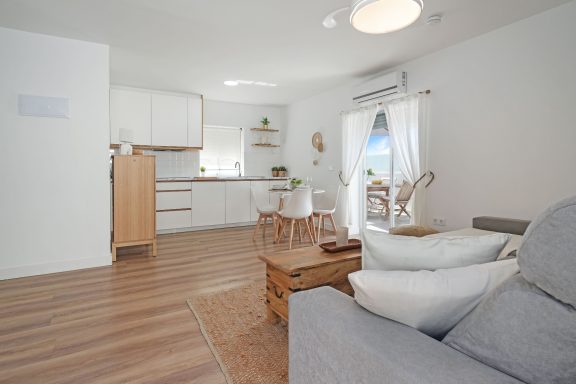 Salón luminoso con una cocina abierta, mesa, sillas y decoración minimalista.