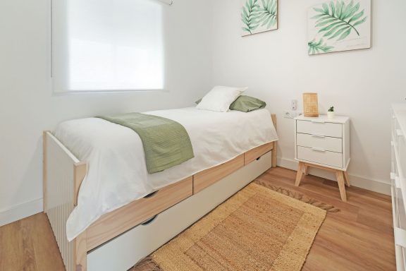 Habitación luminosa con cama individual, mesita de noche y decoración de plantas.