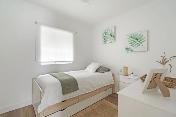 Habitación luminosa con cama blanca, decoración minimalista y plantas en las paredes.