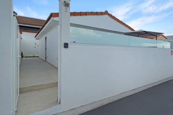 Entrada a una casa moderna, con pared blanca y vidrio, al fondo un cielo despejado.