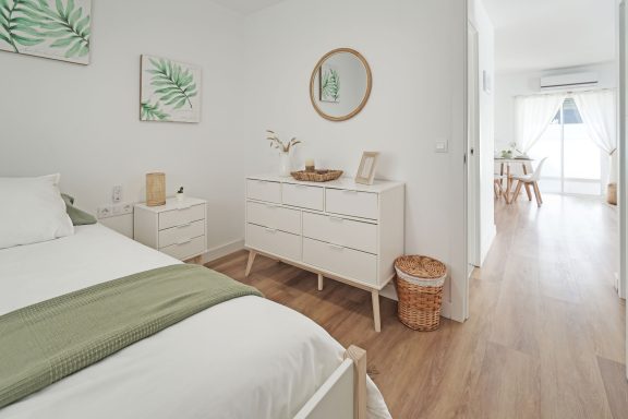 Habitación luminosa con cama, muebles blancos y decoración de plantas.