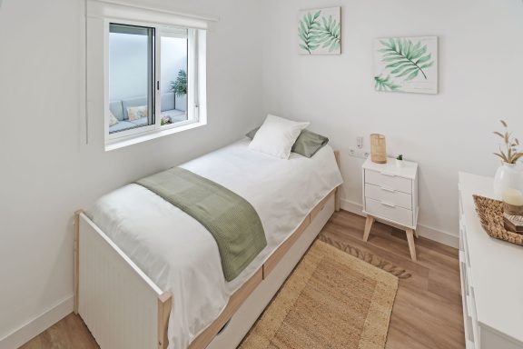 Habitación luminosa con cama individual, mesita y decoraciones de plantas.