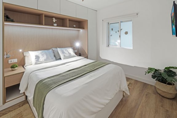 Dormitorio luminoso con cama doble, decorado en tonos neutros y planta junto a la ventana.