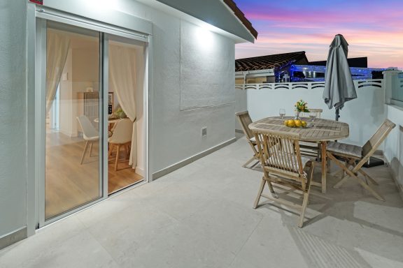 Terraza luminosa con mesa y sillas, decorada con frutas, al atardecer.