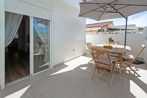 Terraza luminosa con mesa de madera y sombrilla, rodeada de paredes blancas.