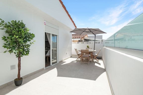 Terraza luminosa con mesa, sillas, sombrilla y planta decorativa. cielo azul.