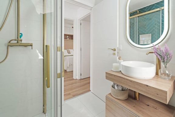 Baño moderno con ducha, lavabo sobre mesa de madera y decoración en tonos claros.