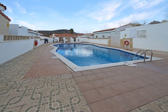 Piscina rodeada de casas, con escaleras y áreas de cerámica a su alrededor.