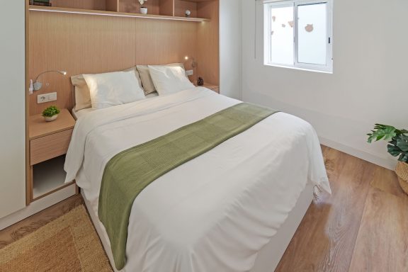 Habitación con cama doble, ropa de cama blanca y verde, y ventana iluminada.